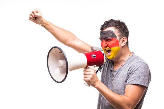 Il fan fedele del sostenitore dell'uomo bello della squadra nazionale della Germania con la faccia dipinta della bandiera ottiene la vittoria felice che grida nel megafono con la mano appuntita. Fans le emozioni.