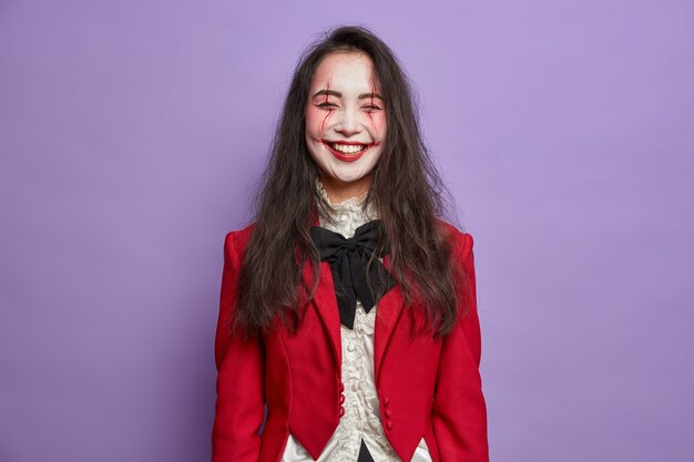 Il fantasma della donna felice felicissima celebra halloween indossa un trucco orribile vestito in costume di carnevale pose contro il muro viola