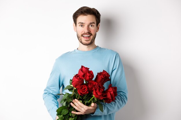 Il fidanzato romantico porta un bellissimo mazzo di rose rosse il giorno di San Valentino, ha un appuntamento con la fidanzata, dice ti amo, in piedi appassionato su sfondo bianco