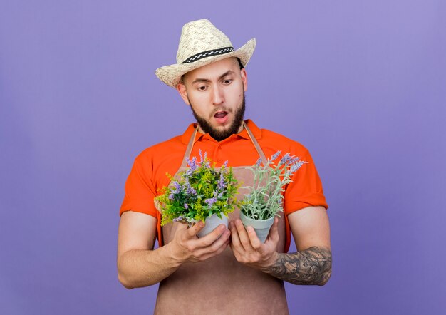 Il giardiniere maschio scioccato che porta il cappello di giardinaggio tiene e guarda i vasi da fiori