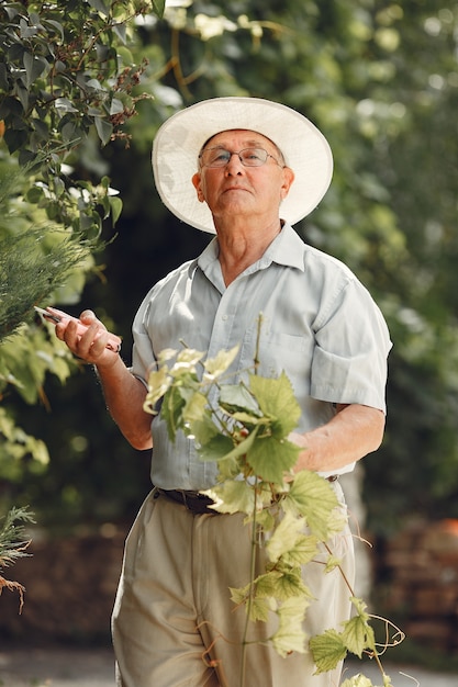 Il giardiniere senior sta godendo il suo lavoro in giardino. Vecchio con una camicia bianca.