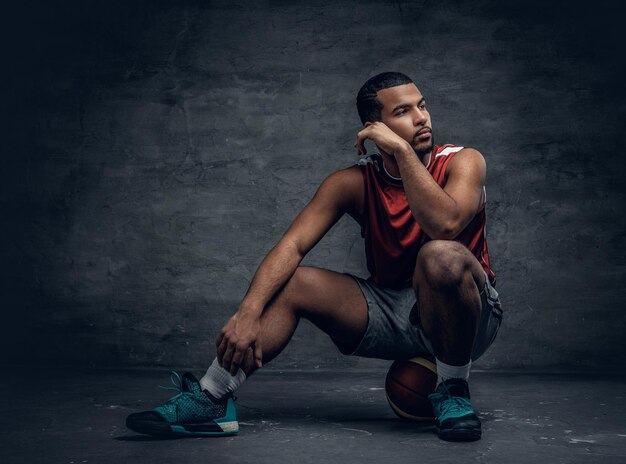 Il giocatore di basket nero si siede su una palla sdraiata su un pavimento.