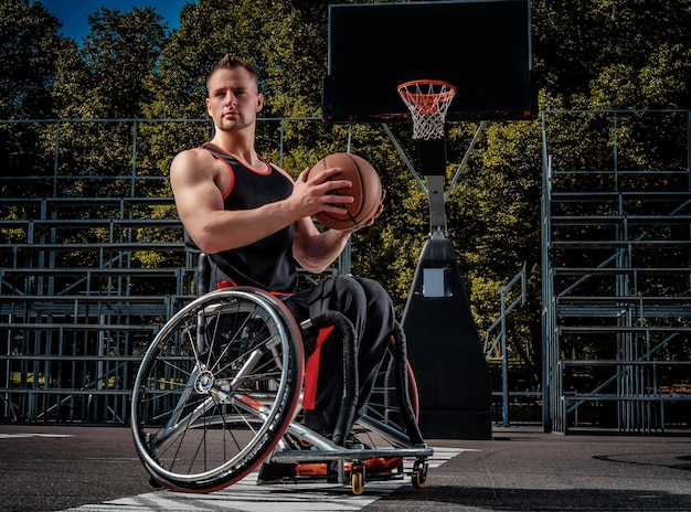 Il giocatore di basket storpio su una sedia a rotelle tiene una palla su un terreno di gioco aperto.