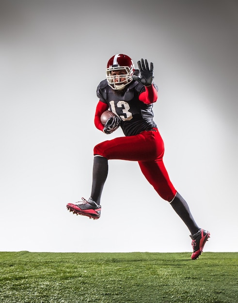 Il giocatore di football americano in azione su erba verde e sfondo grigio.