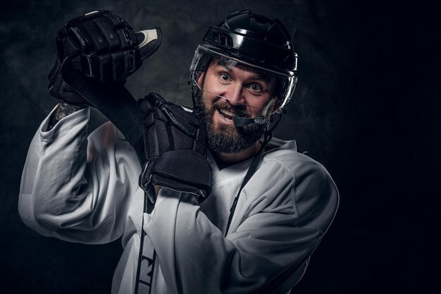 Il giocatore di hockey felice e allegro ha una sessione fotografica in uno studio fotografico scuro.