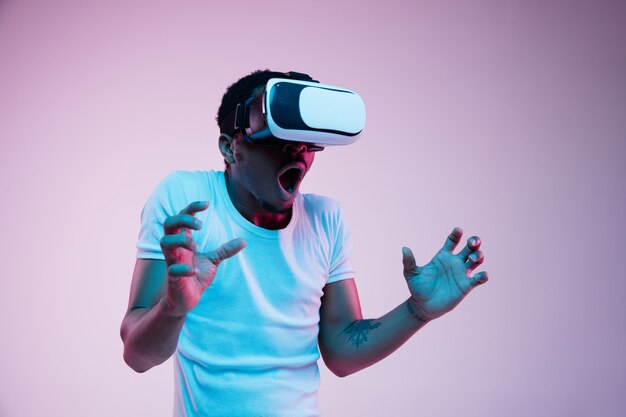 Il giovane afroamericano sta giocando con gli occhiali VR alla luce al neon su gradiente