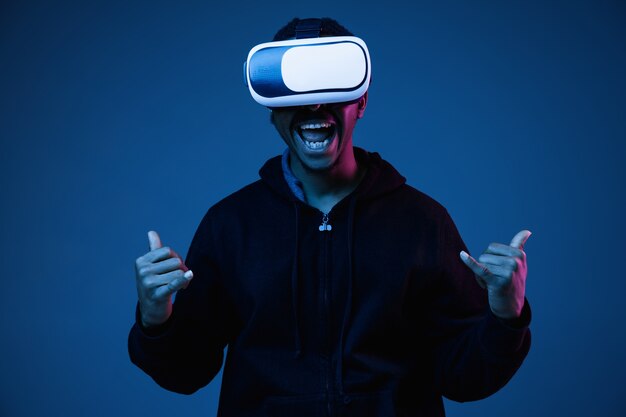 Il giovane afroamericano sta giocando con gli occhiali VR alla luce al neon su gradiente