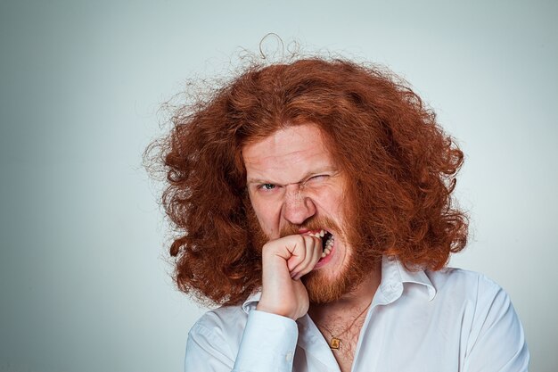 Il giovane arrabbiato con lunghi capelli rossi che si morde le dita