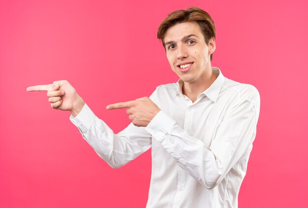 Il giovane bel ragazzo sorridente che indossa una camicia bianca punta a lato isolato sul muro rosa