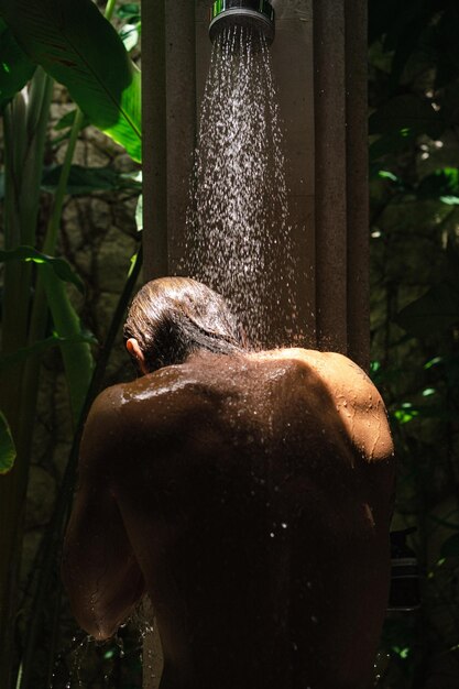 Il giovane bell'uomo si lava sotto la doccia, la corporatura atletica, i tatuaggi.
