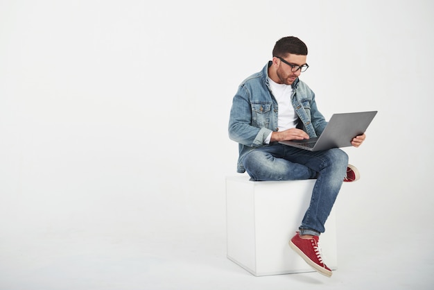 Il giovane bello con il computer portatile e controlla il suo orario su bianco