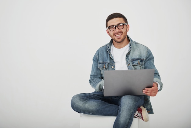 Il giovane bello con il computer portatile e controlla il suo orario su bianco