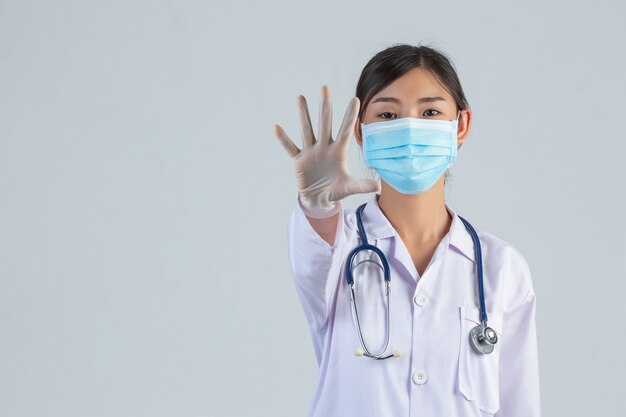 Il giovane bello medico sta indossando la maschera mentre faceva la mano di arresto sulla parete bianca.