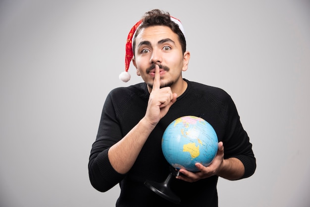 Il giovane con il globo nel cappello di Babbo Natale mostra un gesto di silenzio.