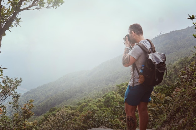 Il giovane con lo zaino sta scattando foto della bellissima natura sulla sua macchina fotografica durante le escursioni in montagna.