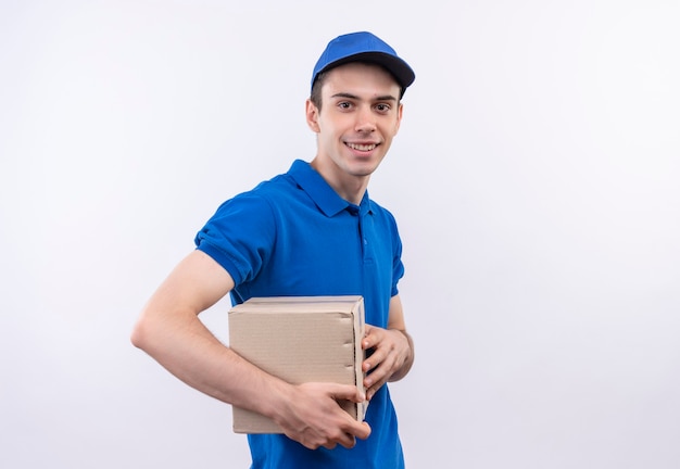 Il giovane corriere che indossa l'uniforme blu e il berretto blu sorride e tiene le scatole