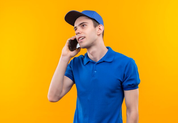 Il giovane corriere che indossa l'uniforme blu e il cappuccio blu parla sul telefono