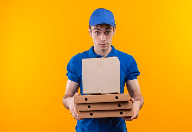 Il giovane corriere che indossa l'uniforme blu e il cappuccio blu tiene le scatole