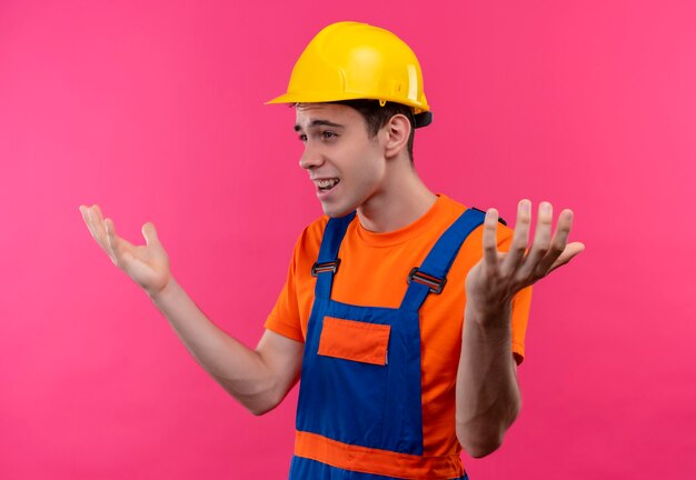 Il giovane costruttore che indossa l'uniforme della costruzione e il casco di sicurezza è sorpreso