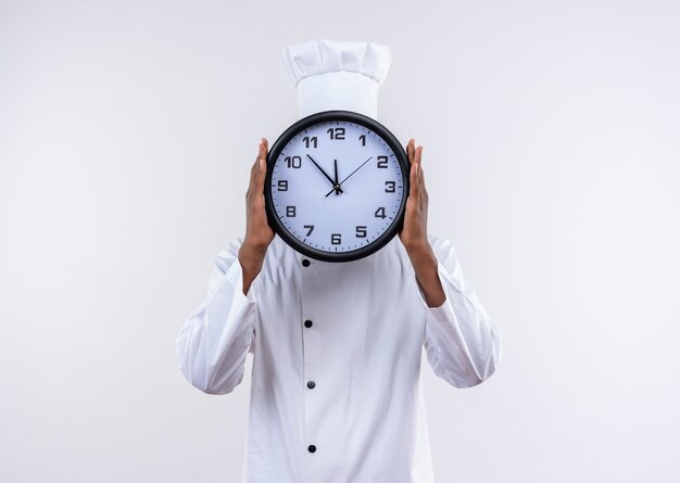 Il giovane cuoco afroamericano in uniforme del cuoco unico chiude il fronte con l'orologio isolato su fondo bianco con lo spazio della copia