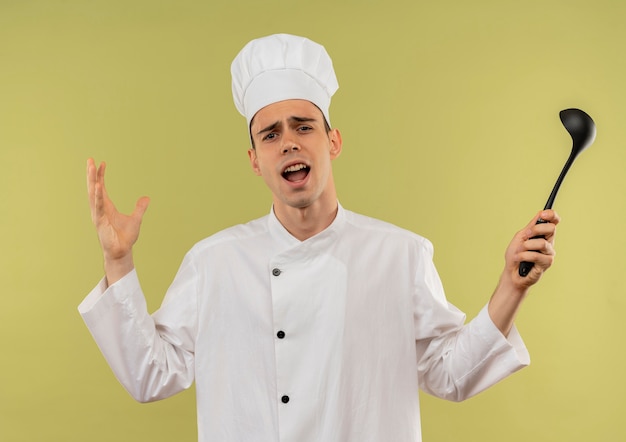 Il giovane cuoco maschio dispiaciuto che porta l'uniforme del cuoco unico si diffonde le mani che tengono il mestolo