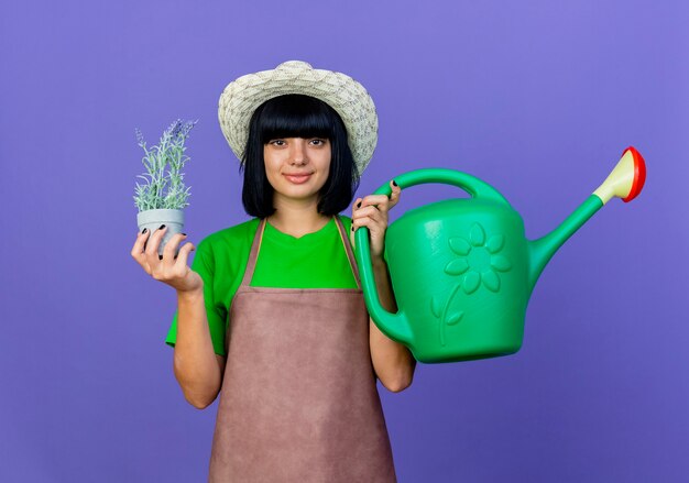 Il giovane giardiniere femminile piacevole in uniforme tiene l'annaffiatoio e il vaso di fiori