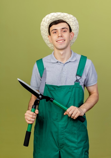 Il giovane giardiniere maschio sorridente che porta il cappello di giardinaggio tiene i clippers