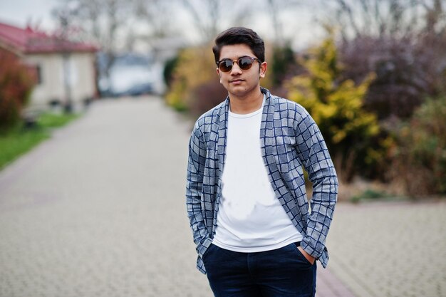 Il giovane indiano alla moda con gli occhiali da sole indossa una posa casual all'aperto