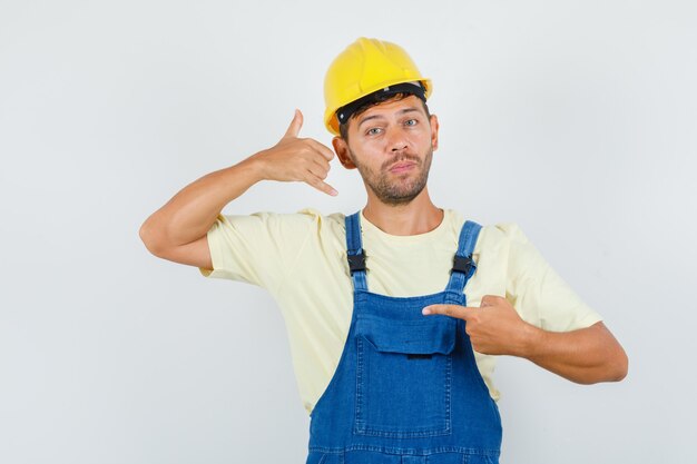 Il giovane ingegnere che mostra una chiamata mi firma nella vista frontale uniforme.