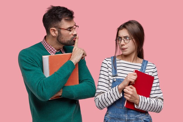 Il giovane insegnante o tutor maschio tiene il vecchio libro di testo rosso, mostra il segno di silenzio, chiede al tirocinante di non diffondere voci