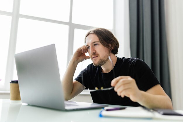 Il giovane lavoratore infelice con gli occhiali guarda lo schermo del laptop scioccato dal guasto del gadget o da problemi operativi Uomo frustrato confuso sorpreso da un errore imprevisto sul dispositivo del computer