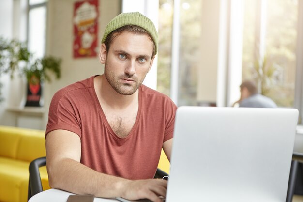 Il giovane manager prospero indossa una maglietta e un cappello casual, lavora su un laptop generico