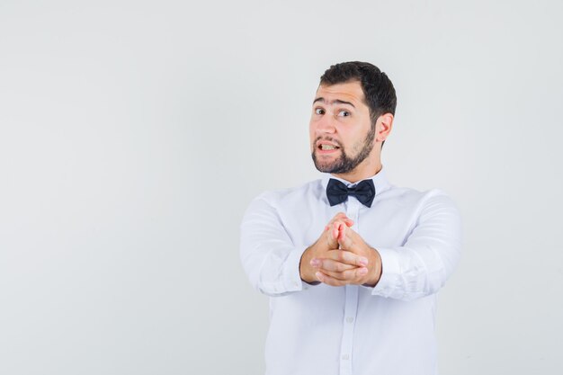 Il giovane maschio che mostra il gesto della pistola ha indicato alla macchina fotografica in camicia bianca e che sembra fiducioso. vista frontale.