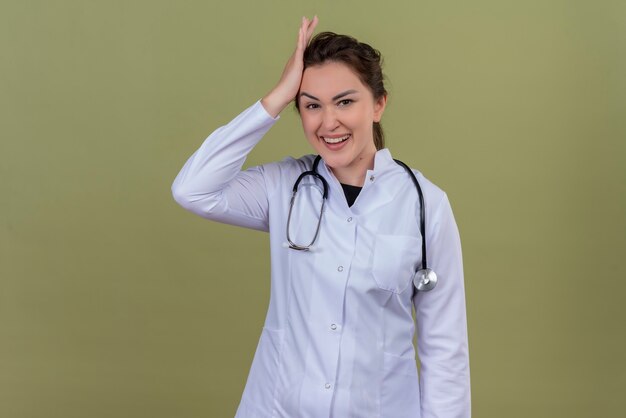 Il giovane medico sorridente che porta lo stetoscopio d'uso dell'abito medico ha messo la sua mano sulla testa sulla parete verde