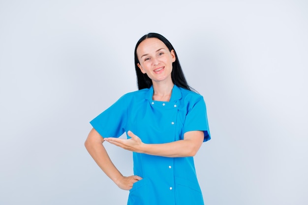 Il giovane medico sorridente sta indicando a sinistra con la mano su fondo bianco