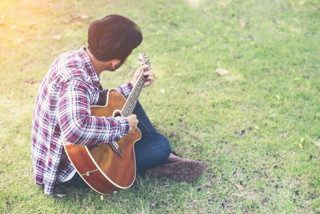 Il giovane pantaloni a vita bassa praticata chitarra nel parco, felice e godere p