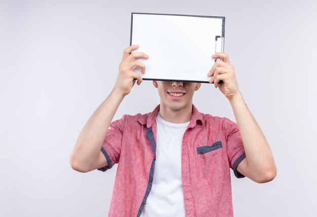 Il giovane ragazzo caucasico sorridente che porta la camicia rosa ha coperto gli occhi con appunti su fondo bianco isolato