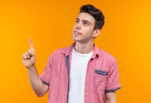 Il giovane ragazzo caucasico sorridente che porta la camicia rosa punta verso l'alto su fondo arancio isolato