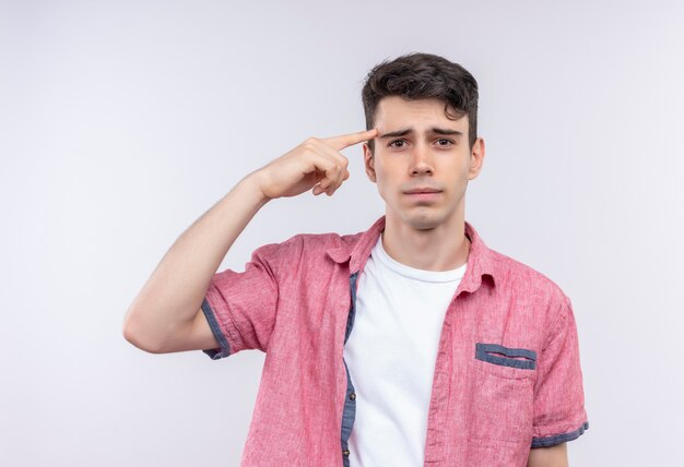 Il giovane ragazzo caucasico triste che porta la camicia rosa ha messo il suo dito sulla fronte su fondo bianco isolato