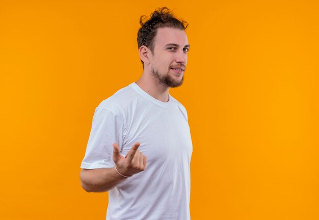 Il giovane ragazzo sorridente che porta la maglietta bianca indica alla macchina fotografica su fondo arancio isolato