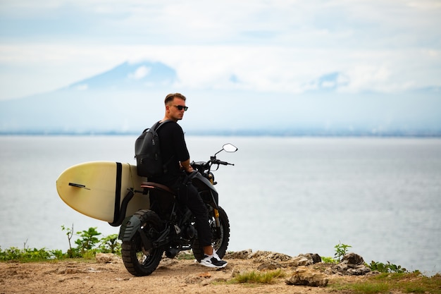 Il giovane si siede su una moto con una tavola da surf