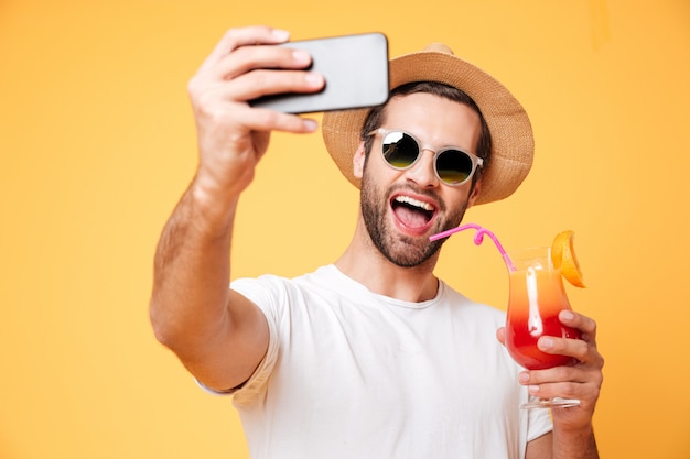 Il giovane sorridente fa il selfie dal cocktail della tenuta del telefono.