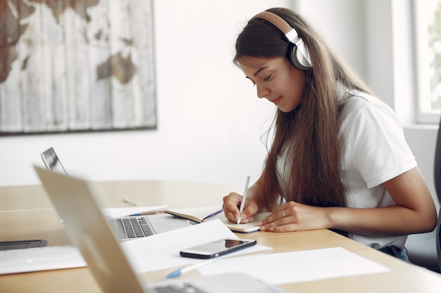 Il giovane studente che si siede alla tavola e usa il computer portatile