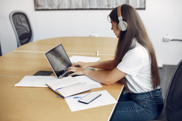 Il giovane studente che si siede alla tavola e usa il computer portatile