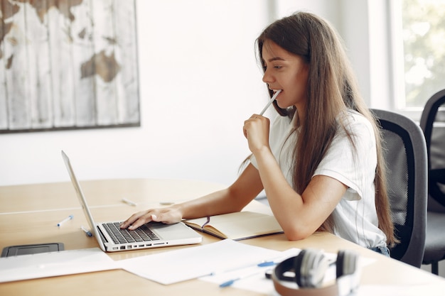 Il giovane studente che si siede alla tavola e usa il computer portatile