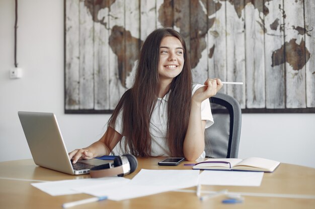 Il giovane studente che si siede alla tavola e usa il computer portatile