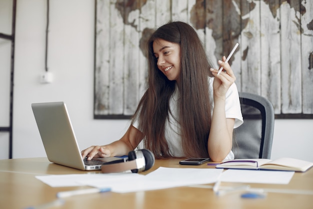 Il giovane studente che si siede alla tavola e usa il computer portatile