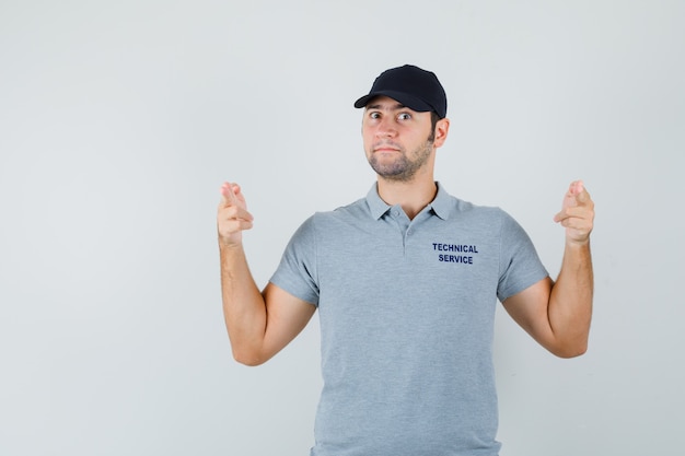 Il giovane tecnico che fa il segno della pistola del dito in uniforme grigia e sembra fiducioso.