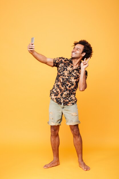 Il giovane uomo africano allegro fa il selfie con il gesto di pace