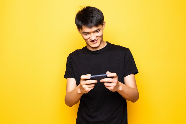 Il giovane uomo asiatico gioca dalla condizione del telefono cellulare isolata sopra la parete gialla